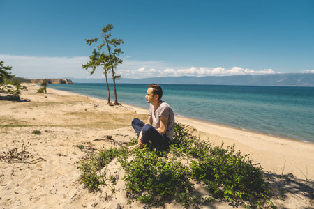 Man traveler relaxing on the beach of Olkhon island overlooking the water of the lake and the...