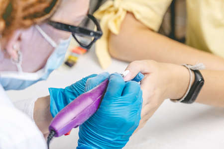 Female manicurist doing manicure hardware cutter removing old varnish in the salon. The concept of beauty professional nail careの写真素材