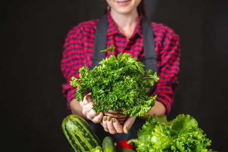 A young woman farmer is holding a box with fresh vegetables and green salad on a dark background. Organic raw products grown on the farm.の写真素材