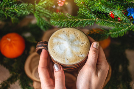 A mug of cappuccino coffee on a wooden background with green branches of a Christmas tree. Warm and...