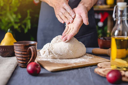A man chef in a black apron kneads the dough with his hands for Christmas baking. Joyful cooking for festive Christmas and new year tableの写真素材