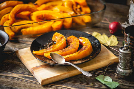 Slices of baked orange pumpkin with honey and cinnamon on a wooden table. Autumn warm dish as a dessertの写真素材