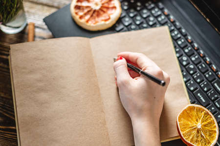 A woman's hand is writing in a notebook dreams plans and goals on a festive wooden background. Christmas message to yourself in the new year.の写真素材