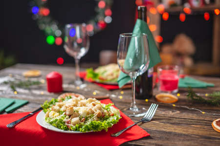 Beautiful festive Christmas table with appetizing green Caesar salad with lettuce leaves and a glass on a red napkin on a wooden tableの写真素材