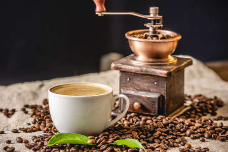 A Cup of coffee with foam and a wooden vintage coffee grinder. Fragrant invigorating drink from freshly roasted coffee beans.の写真素材