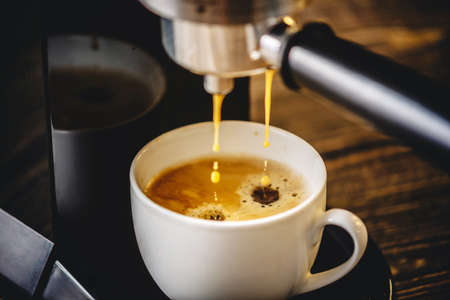 Espresso pours from the coffee machine into a white Cup forming a Golden foamの写真素材