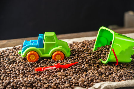 Children's bright toys a bucket with a shovel and a car on a pile of roasted coffee beans like in a...