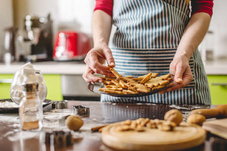Cook housewife making cookies at home on a colorful kitchen. A woman holding a plate with ready Golden freshly baked cookies in the shape of Christmas treesの写真素材