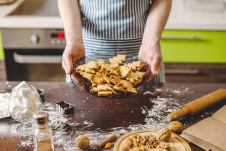 Cook housewife making cookies at home on a colorful kitchen. A woman holding a plate with ready Golden freshly baked cookies in the shape of Christmas treesの写真素材