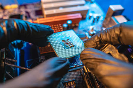 Engineer repairman holding hands in black gloves chip processor, CPU to insert into the socket of the computer motherboard. The concept of technology hardware in the neon lightの素材 [FY310137359389]