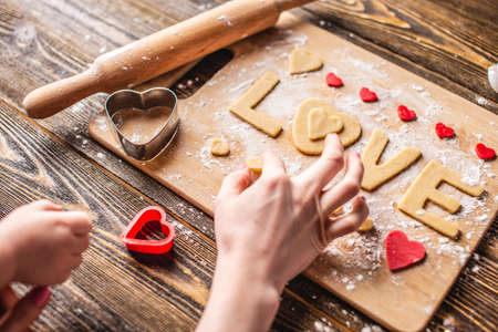 Cooking cookies from the dough in the shape of a heart and the word love on dark wooden background. Baking for Valentine's day and a romantic dateの写真素材