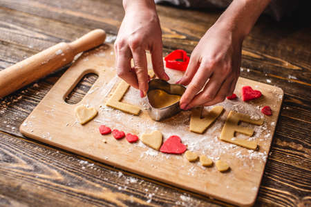 Cooking cookies from the dough in the shape of a heart and the word love on dark wooden background. Baking for Valentine's day and a romantic dateの写真素材