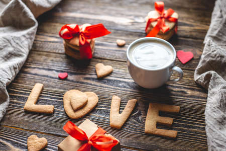 Cup of coffee and a message from a sweet cookie in the form of the word love on a dark wooden background. Romantic Valentine's day giftの写真素材