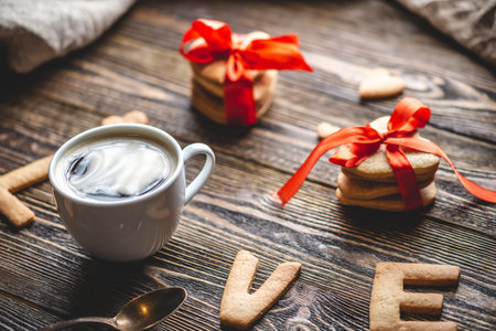 Cup of coffee and a message from a sweet cookie in the form of the word love on a dark wooden background. Romantic Valentine's day giftの写真素材