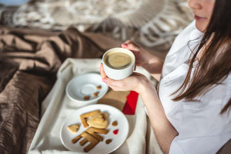 Beautiful young woman have a romantic Breakfast in cozy morning bed. Cup of Coffee and word love from sweet cookies. Surprise on Valentine's dayの写真素材