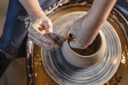 Potter working on a Potter's wheel making a vase. Young woman forming the clay with her hands creating jug in a workshop. Close up. The view from the topの写真素材