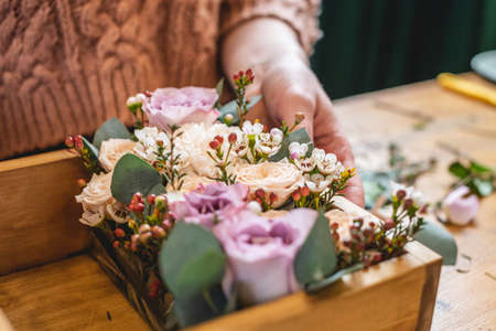Woman florist collects a flower composition in a wooden box with hands. Spring bouquet of roses in pastel colors in a flower shopの写真素材