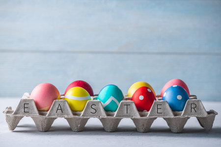Colorful decorated bright Easter eggs in a tray on a wooden background. Festive spring card with...