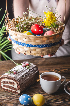 Festive Easter lunch with colorful bright eggs in a basket and an Easter cake on a wooden table....