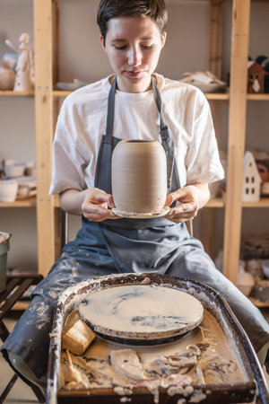Woman potter working on a Potter's wheel making a vase. Master pulls the jug off the circle wetting...