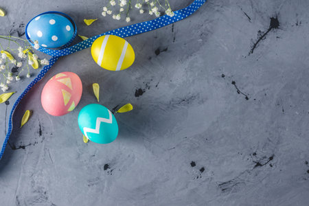 Bright colorful Easter eggs with a ribbon and spring flowers on a gray background. Festive spring...