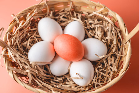 Bright red Easter egg among white ones in a basket on a light background. Festive spring greeting...