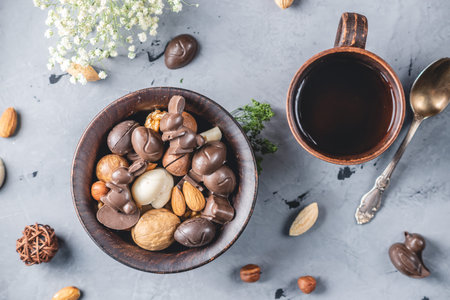 Chocolate in the shape of eggs and rabbits with nuts and cup of tea on a gray background. Festive...