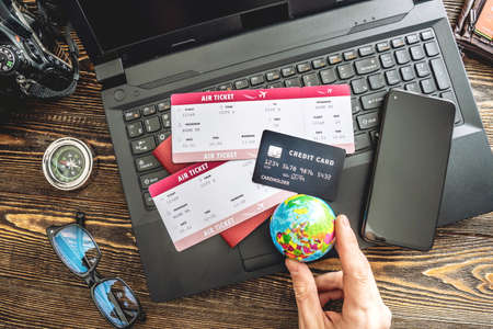 Preparing for an exciting journey. Man books flights by typing on a laptop and paying with a credit card on a wooden background. The view from the top.の写真素材