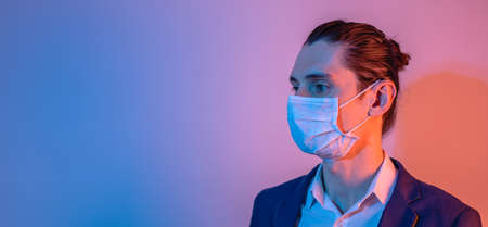 Portrait of a male businessman in a medical mask in dramatic neon light. Crisis for business during the pandemic.の写真素材