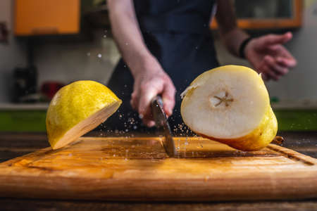 Chef cutting a yellow ripe pear in half with a large knife in motion. Splashes of water and juice fly in different directions and freeze in the airの写真素材