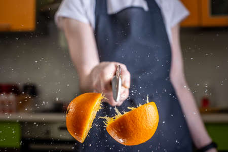 Chef cutting an orange in half with a large knife in motion. Splashes of water and juice fly in different directions and freeze in the airの写真素材
