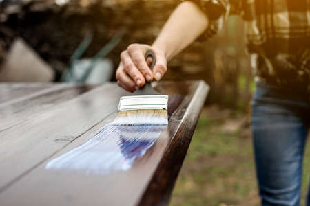 A wood carpenter applies a protective layer of transparent varnish. Hand with a brush close up on the table topの写真素材