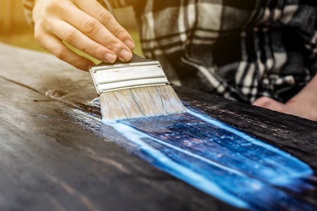 A wood carpenter applies a protective layer of transparent varnish. Hand with a brush close up on...