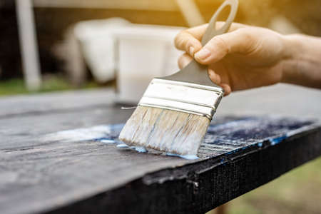 A wood carpenter applies a protective layer of transparent varnish. Hand with a brush close up on the table topの写真素材