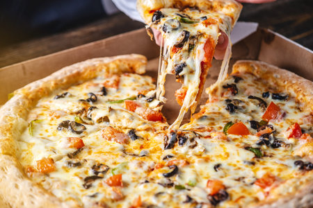 A slice of fresh hot vegetarian pizza with a stretch of mozzarella cheese in the cook's hand.