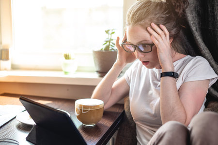A young beautiful woman reading interesting news on the Internet using a gadget tablet sitting at a...