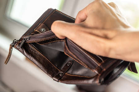 The man is holding an open empty brown leather wallet purse. The concept of economic crisis and business bankruptcy in the post-pandemic periodの写真素材