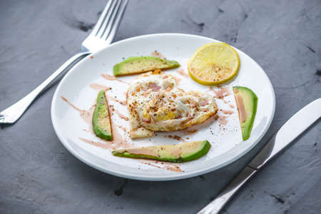 A beautiful healthy romantic Breakfast of fried eggs in the shape of a heart with slices of avocado and lemon on a white plate.の写真素材