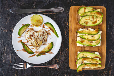 A beautiful healthy romantic Breakfast of fried eggs in the shape of a heart on a white plate and avocado sandwiches. The view from the topの写真素材