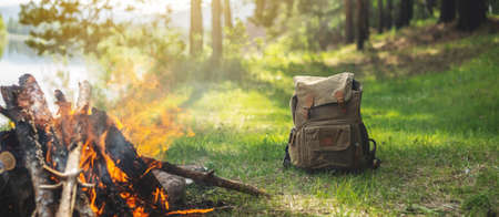 Hiking backpack in the forest on the river shore by the bonfire. A wonderful sunny weekend in nature. A quiet and picturesque place for reflection and relaxation.の写真素材