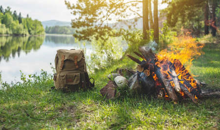 Hiking backpack in the forest on the river shore by the bonfire. A wonderful sunny weekend in nature. A quiet and picturesque place for reflection and relaxation.の写真素材