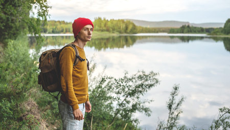 A tourist traveler with a backpack and a red hat are standing by the river with a beautiful...
