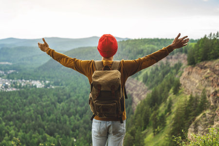 A tourist traveler with a backpack and a red hat is standing on the edge of a cliff in front of a...