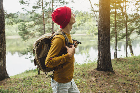 A tourist with a backpack and a red hat is walking in the forest among the trees. The concept of...