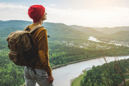 A tourist traveler with a backpack and a red hat is standing on the edge of a cliff and is looking...