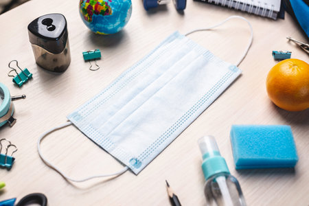 Stationery school supplies around the medical mask on the desk. Top view. Back to school concept.