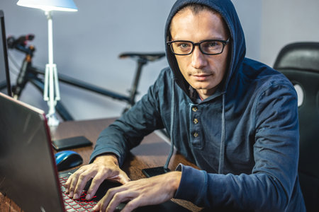 Man hacker in the hood is programming virus code at the keyboard for the laptop. The concept of...