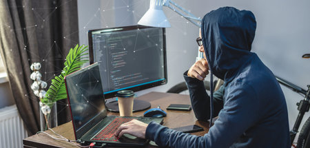 Man hacker in a hood are programming virus code on a laptop. The concept of Internet fraud and...