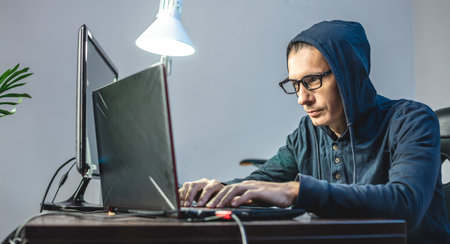 Man hacker in the hood is programming virus code at the keyboard for the laptop. The concept of...