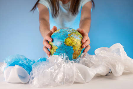 A woman is pulling out an Earth in form globe of a pile of plastic garbage. Concept of environmental pollution and saving the planetの写真素材